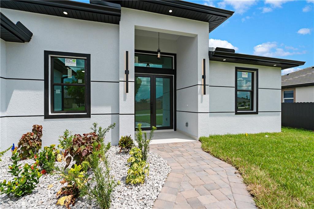 Contemporary exterior with stucco finish, black-framed windows, double glass entry doors, and a paver walkway