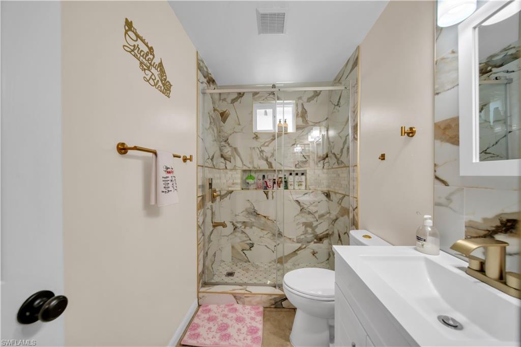 Step-in shower with clear glass enclosure, marble-style tile surround, and built-in shelving