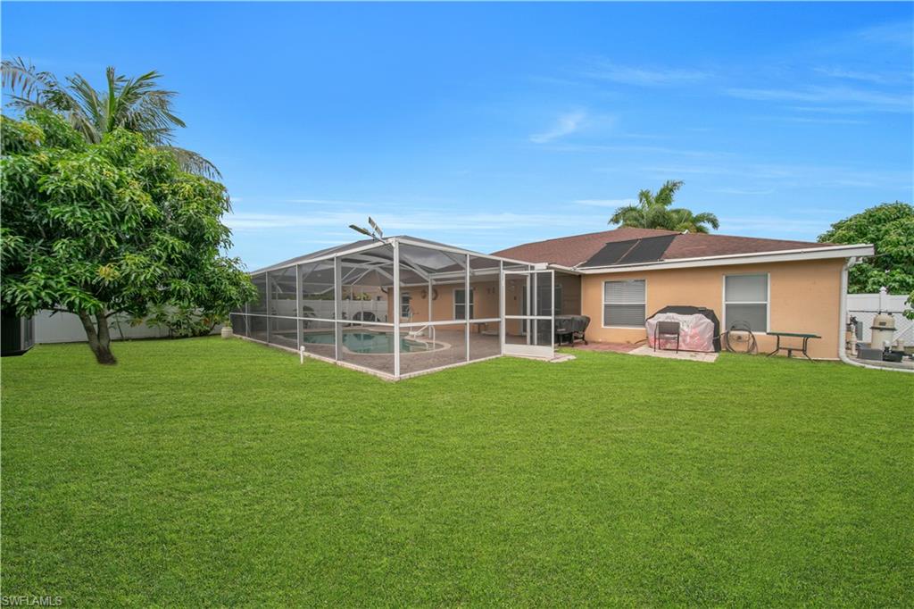 Expansive green lawn, screened-in swimming pool enclosure, stucco exterior, brown shingle roof, solar panels