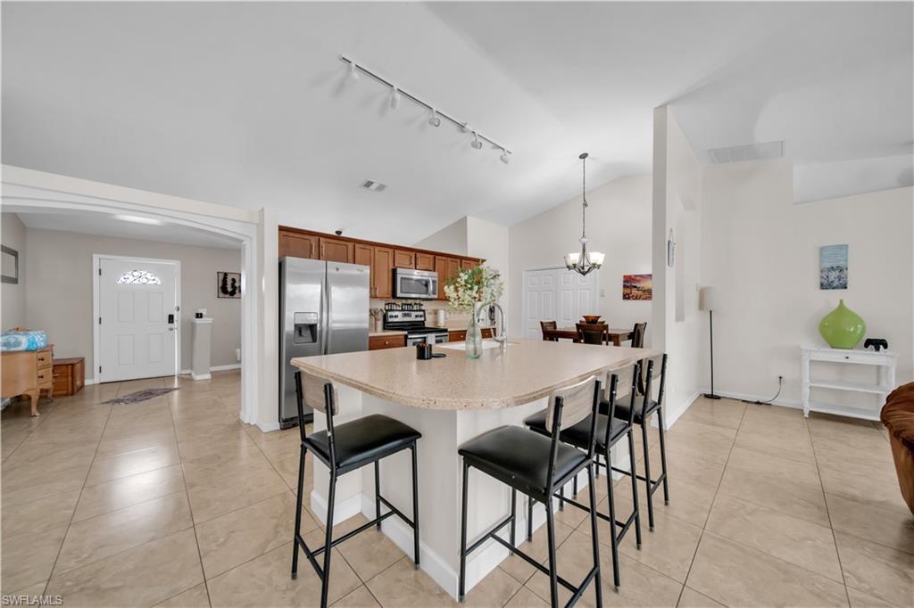 Spacious kitchen featuring an island with seating, stainless steel appliances, wood cabinetry, and tile flooring throughout