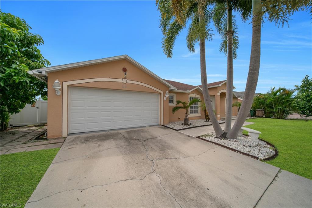 Stucco exterior featuring an attached garage, a paved driveway, and mature palm trees