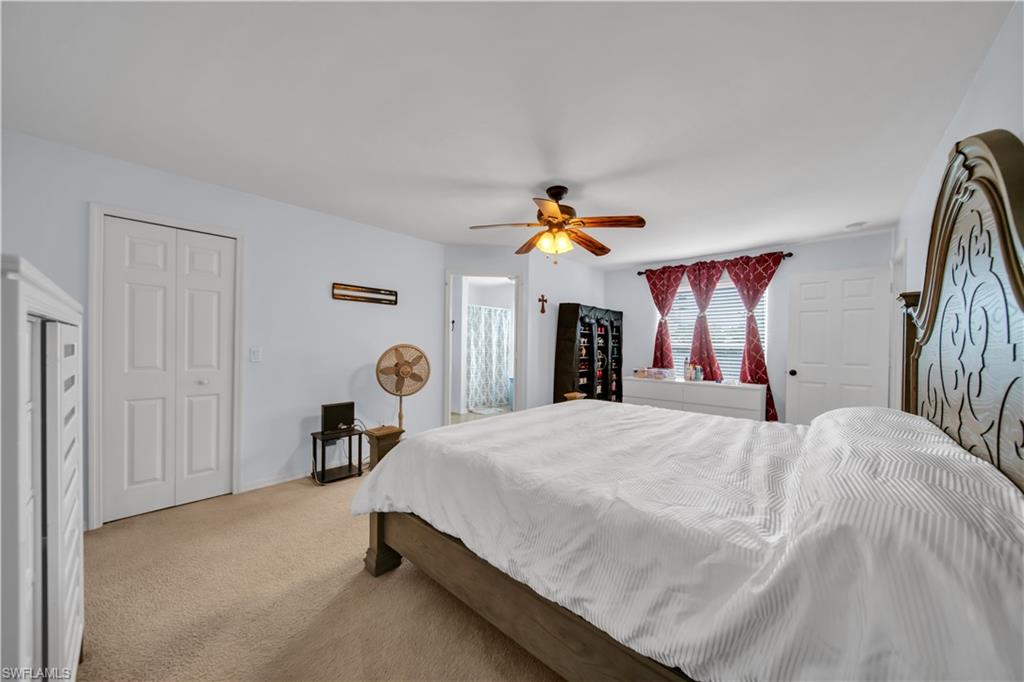 Carpeted bedroom featuring a ceiling fan with integrated lighting, white bi-fold closet doors, and multiple windows