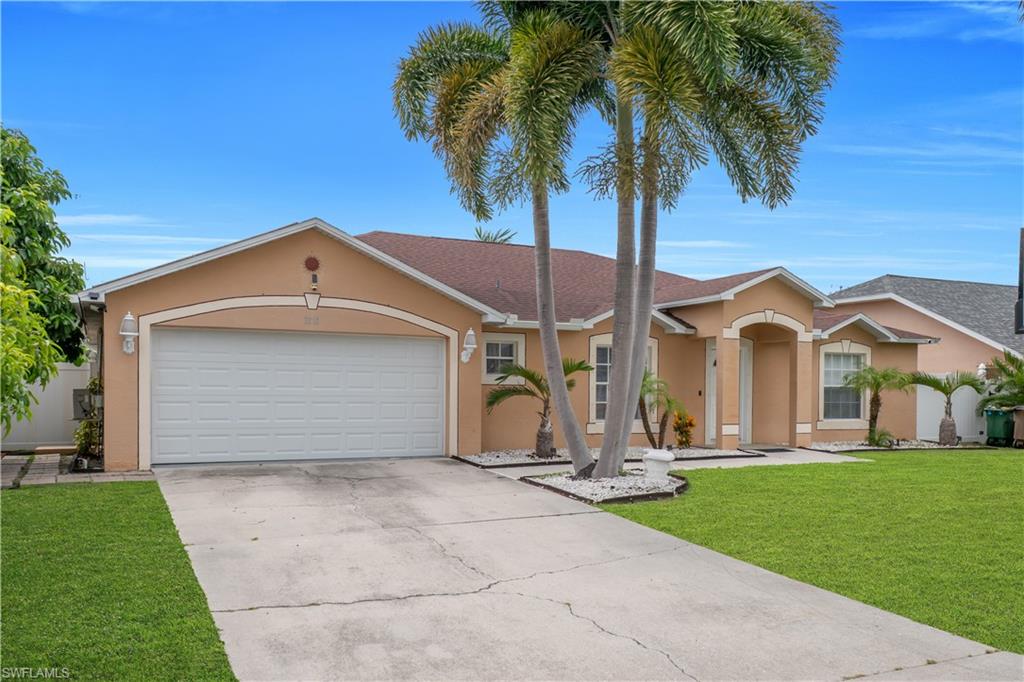 Stucco exterior with arched entryway, attached garage, concrete driveway, manicured lawn, and mature palm trees