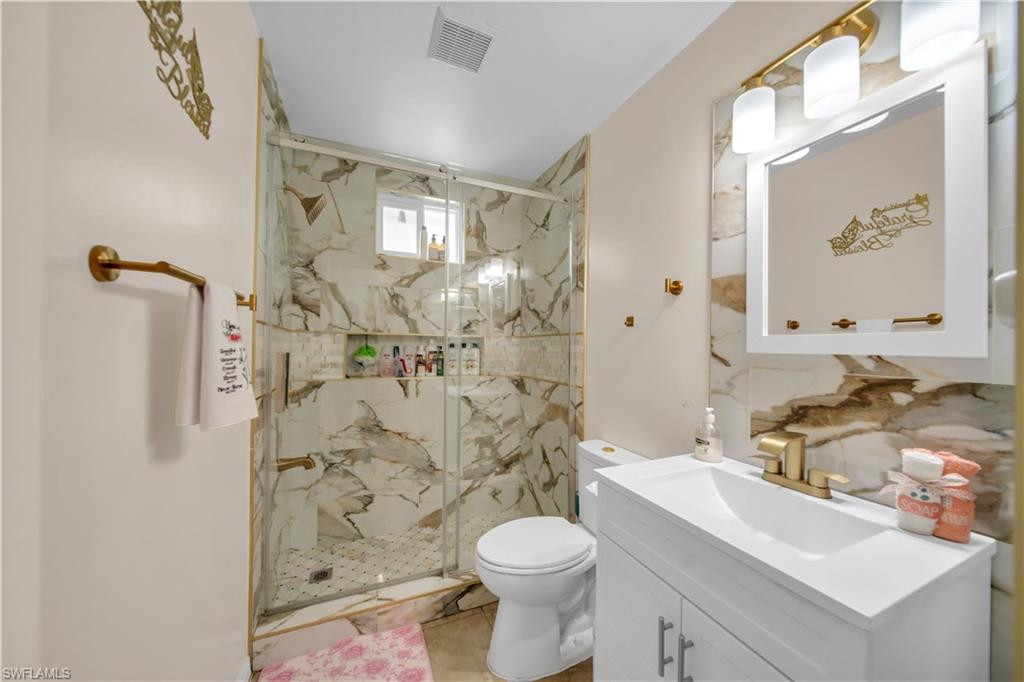 Shower with glass enclosure, white vanity with integrated sink, gold-finish fixtures, wall-mounted mirror, and patterned wall tile