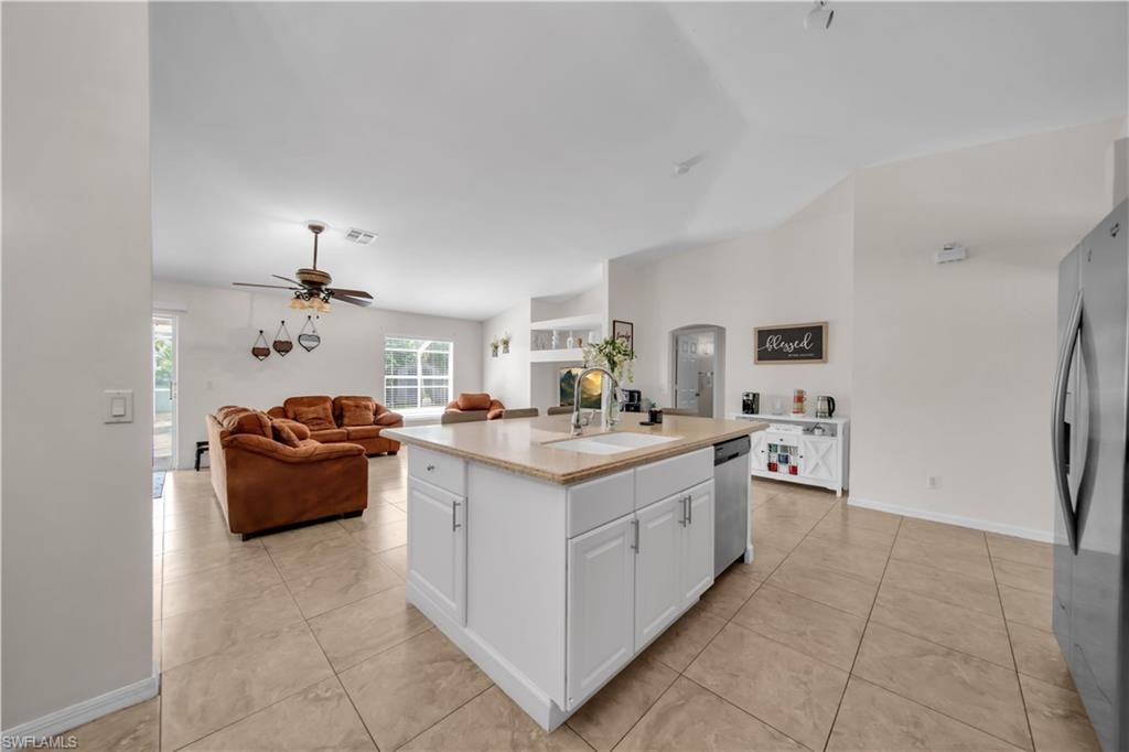 Kitchen island with an undermount sink and white cabinetry, stainless steel dishwasher, tile flooring, and vaulted ceilings