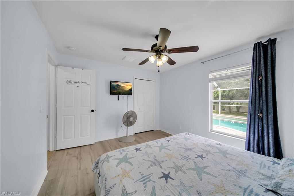 Light wood-finish flooring, ceiling fan with integrated lighting, white paneled doors, and a window with blinds