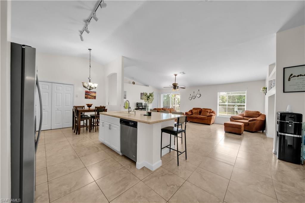 Open-concept living area featuring a kitchen island with seating, tile flooring, vaulted ceilings, and large windows