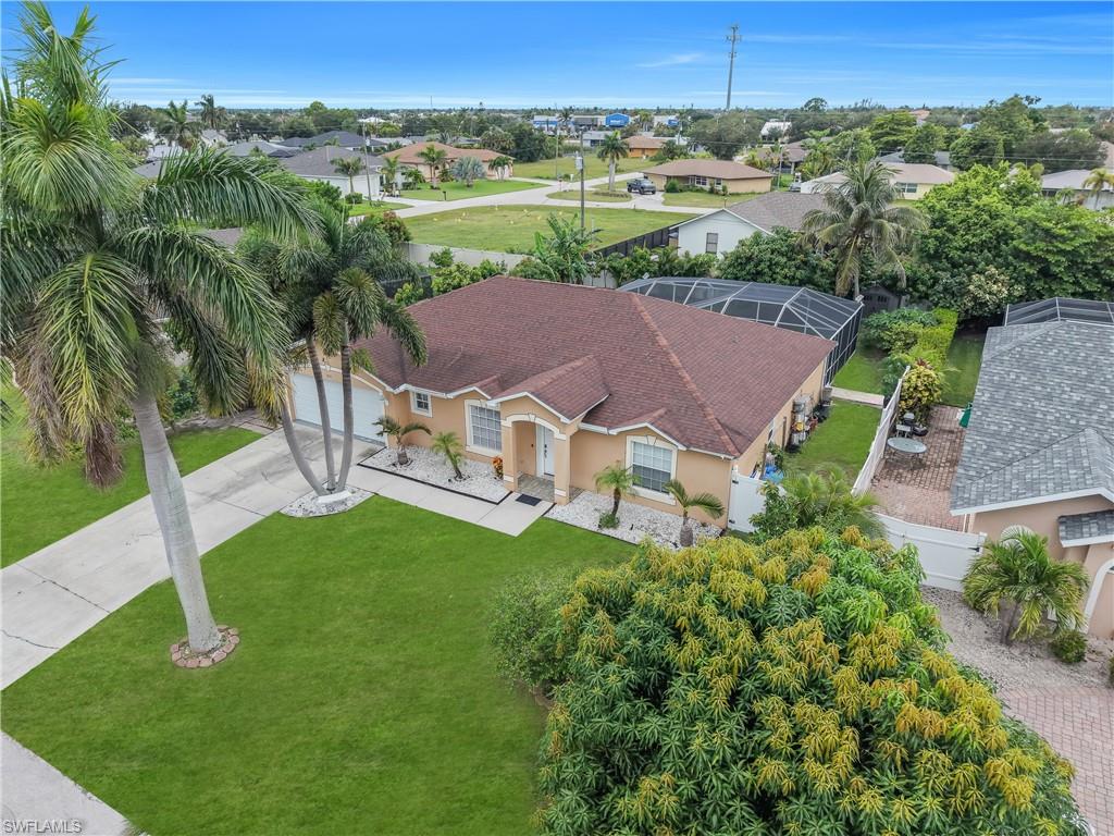 Stucco exterior with a hip roof, featuring a screened enclosure, mature palm trees, and a concrete driveway