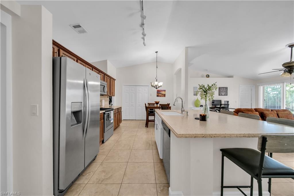 Kitchen featuring stainless steel appliances, wood cabinetry, tile flooring, and a central island with a sink