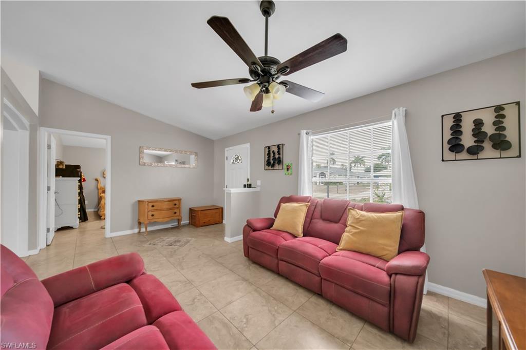 Vaulted ceiling, ceiling fan with integrated lighting, tiled flooring, front door with decorative glass, and a large window