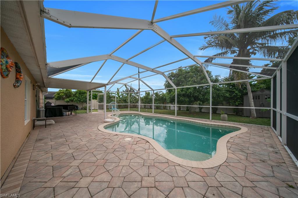 Screened enclosure featuring a freeform swimming pool, extensive paver patio, and covered outdoor living area