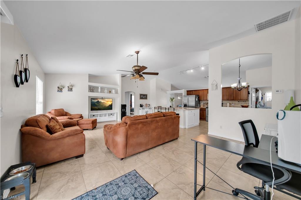 Vaulted ceilings, recessed display shelving, ceiling fan with integrated lighting, tile flooring, and an archway opening to the kitchen