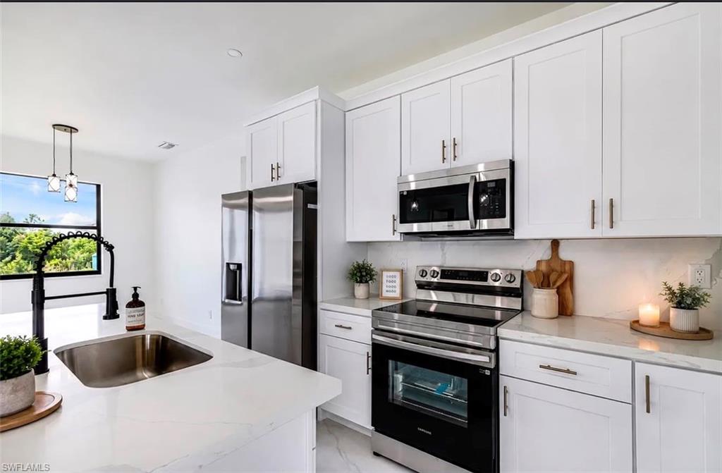 Kitchen featuring white cabinetry, stainless steel appliances, a large window, a stainless steel sink, and light-toned countertops