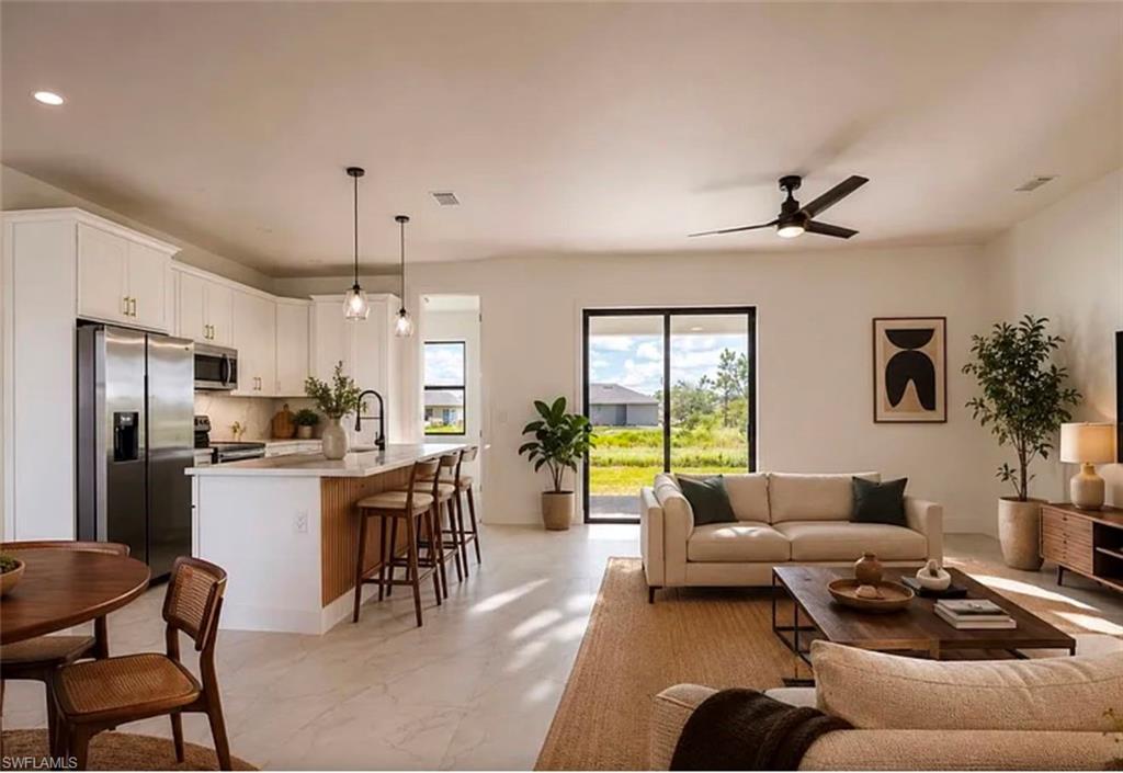 Open-concept living space featuring a kitchen island with seating, stainless steel appliances, a ceiling fan, and sliding glass doors