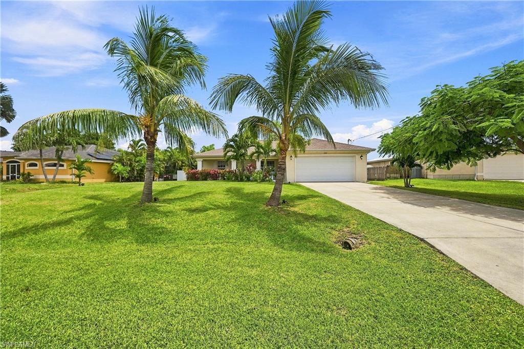 Manicured lawn with mature palm trees, concrete driveway, and attached two-car garage