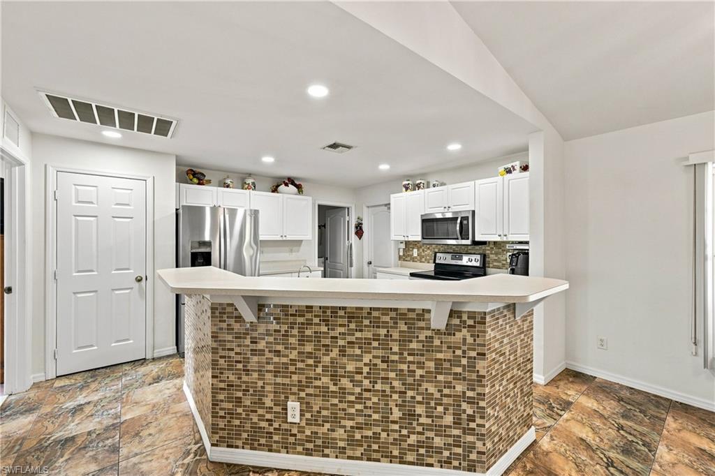 Kitchen featuring white cabinetry, stainless steel appliances, mosaic tile backsplash, and a breakfast bar with a solid surface countertop