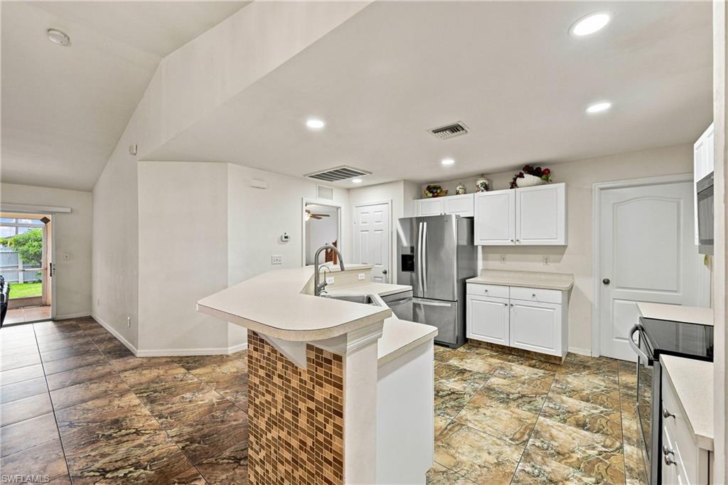 Kitchen featuring tile flooring, white cabinetry, a stainless steel refrigerator, and a breakfast bar with a mosaic tile accent