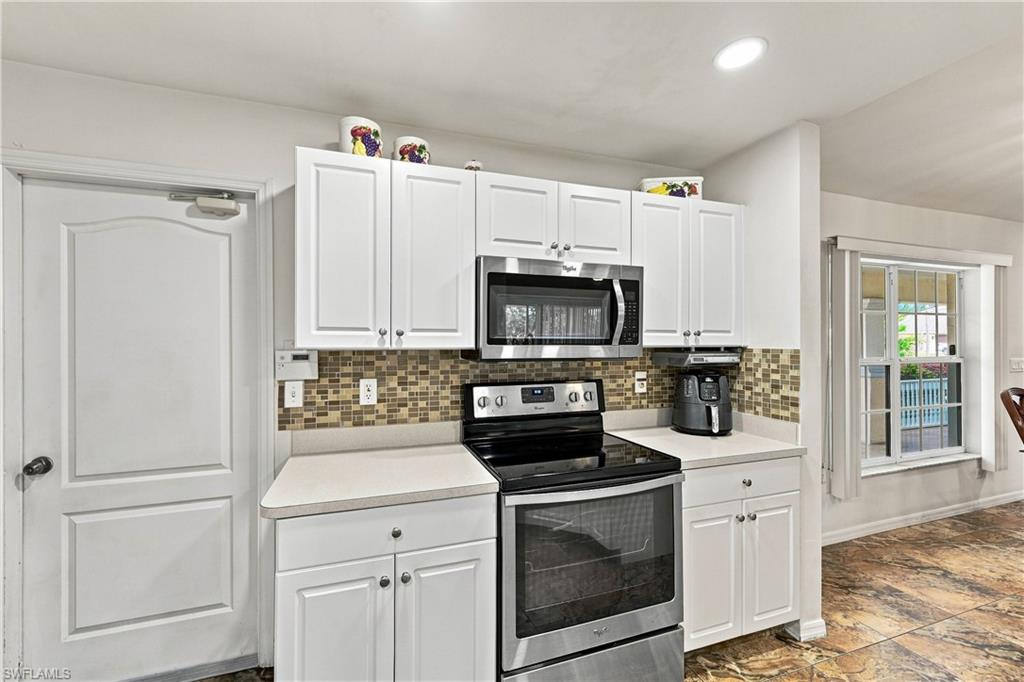 White cabinetry with brushed nickel hardware, stainless steel appliances, mosaic tile backsplash, light-toned countertops, and recessed lighting