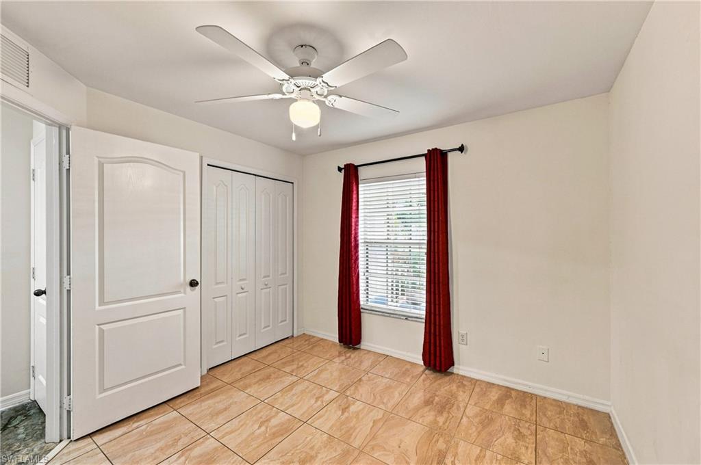 White ceiling fan with integrated lighting, tiled flooring, white bi-fold closet doors, and a window with blinds