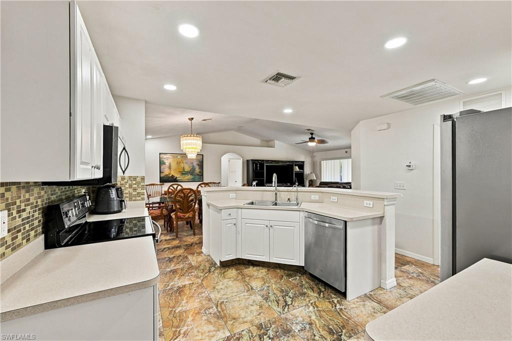 Open-concept kitchen featuring white cabinetry, stone-finish flooring, a stainless steel dishwasher, a kitchen island with sink, and recessed lighting