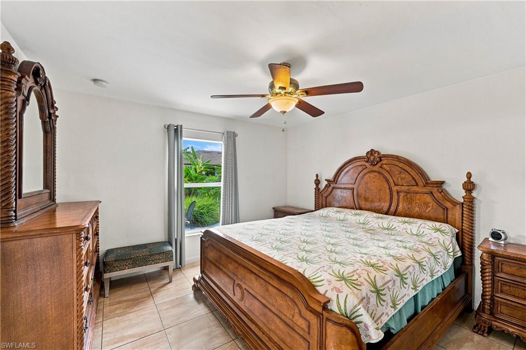 White walls, ceiling fan with light fixture, window with curtains, and tile flooring