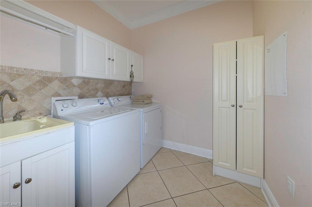 Spacious laundry room features large tile flooring, crown molding, laundry sink, tile backsplash, cabinets, washer, dryer & storage closet.