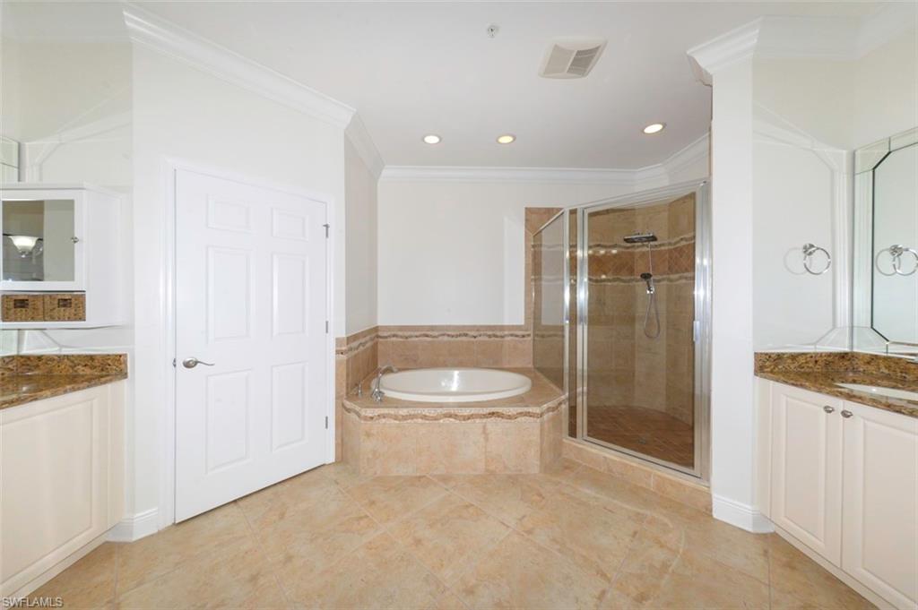 Luxurious primary bathroom with Crown molding, upgraded tile flooring, soaking tub & walk-in shower with upgraded tile and listello, private water closet, separate vanities with granite counters & custom mirrors and lighting.