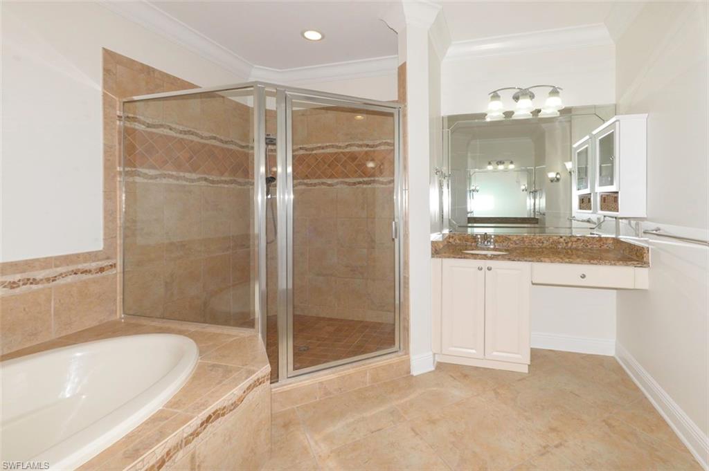 Luxurious primary bathroom with Crown molding, upgraded tile flooring, soaking tub & walk-in shower with upgraded tile and listello, private water closet, separate vanities with granite counters & custom mirrors and lighting.