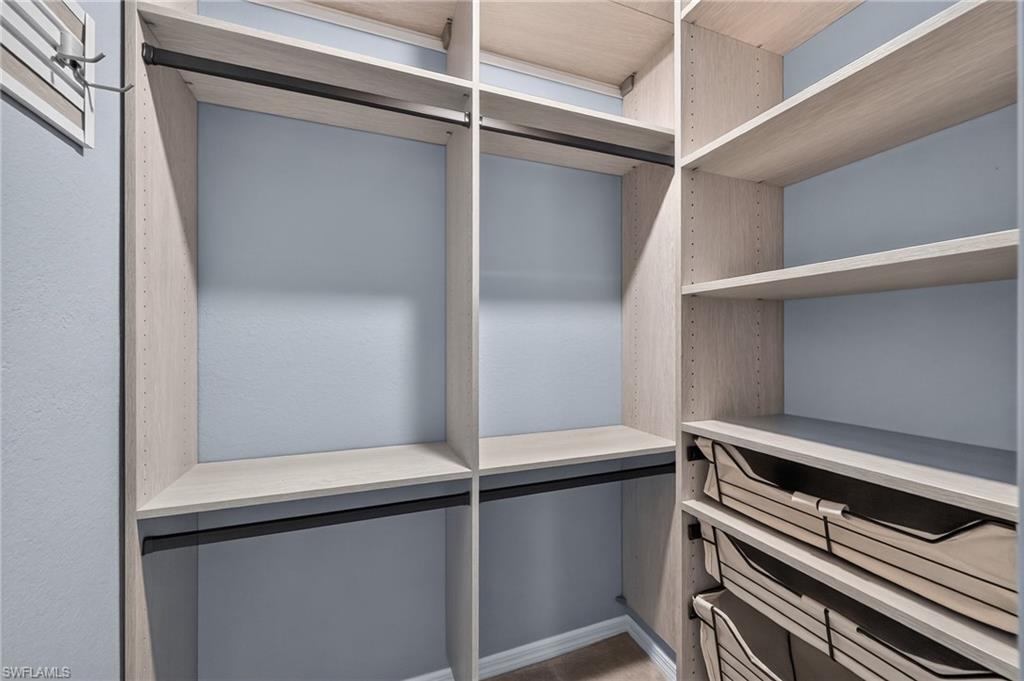 Spacious walk-in closet featuring custom shelving with wood-finish surfaces, mirrored sliding doors, integrated drawer storage with soft-close hardware, and recessed lighting throughout