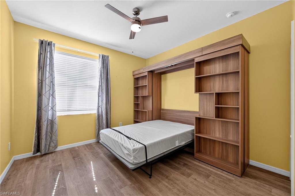 Wood-finish flooring, built-in murphy bed, integrated shelving, ceiling fan, and window with blinds
