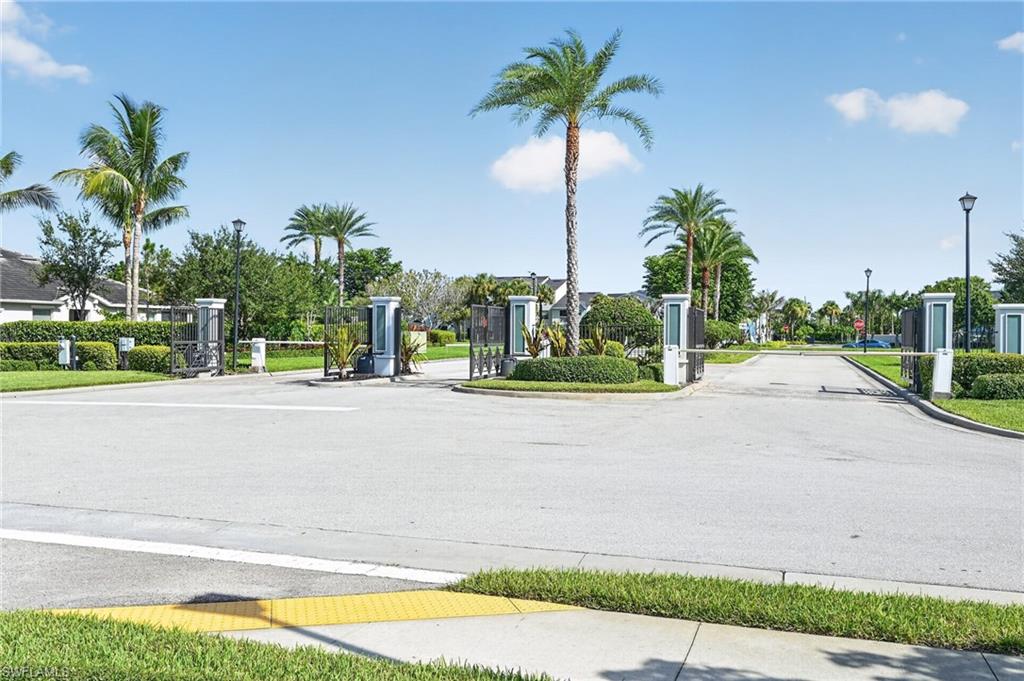 Gated entrance with multiple access lanes, featuring manicured landscaping and mature palm trees