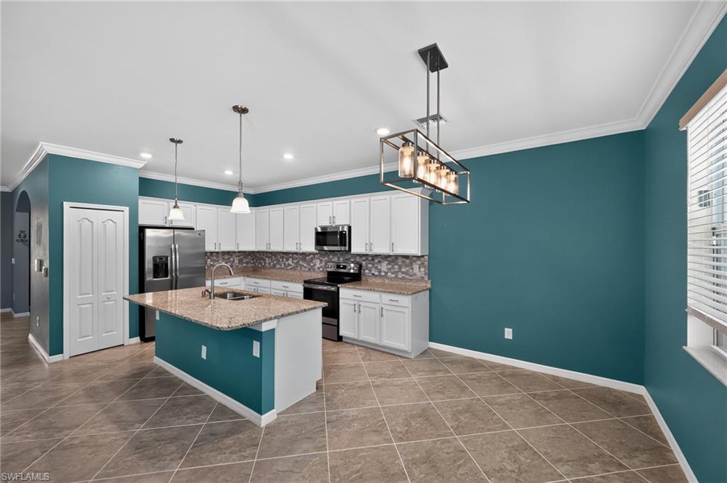 Spacious kitchen featuring white cabinetry, granite-look countertops, black stainless steel appliances, a large center island with breakfast bar seating, pendant lighting, recessed ceiling lights, and a geometric tile floor