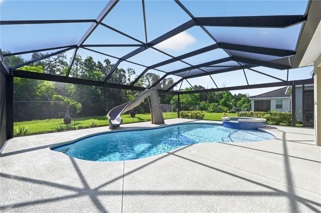Screened-in outdoor pool area featuring a freeform pool, integrated spa with mosaic tile, and a pool slide