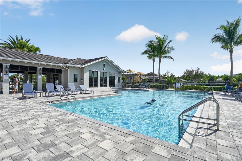 Community pool featuring a stone paver deck, stainless steel pool rails, and an adjacent clubhouse with large windows