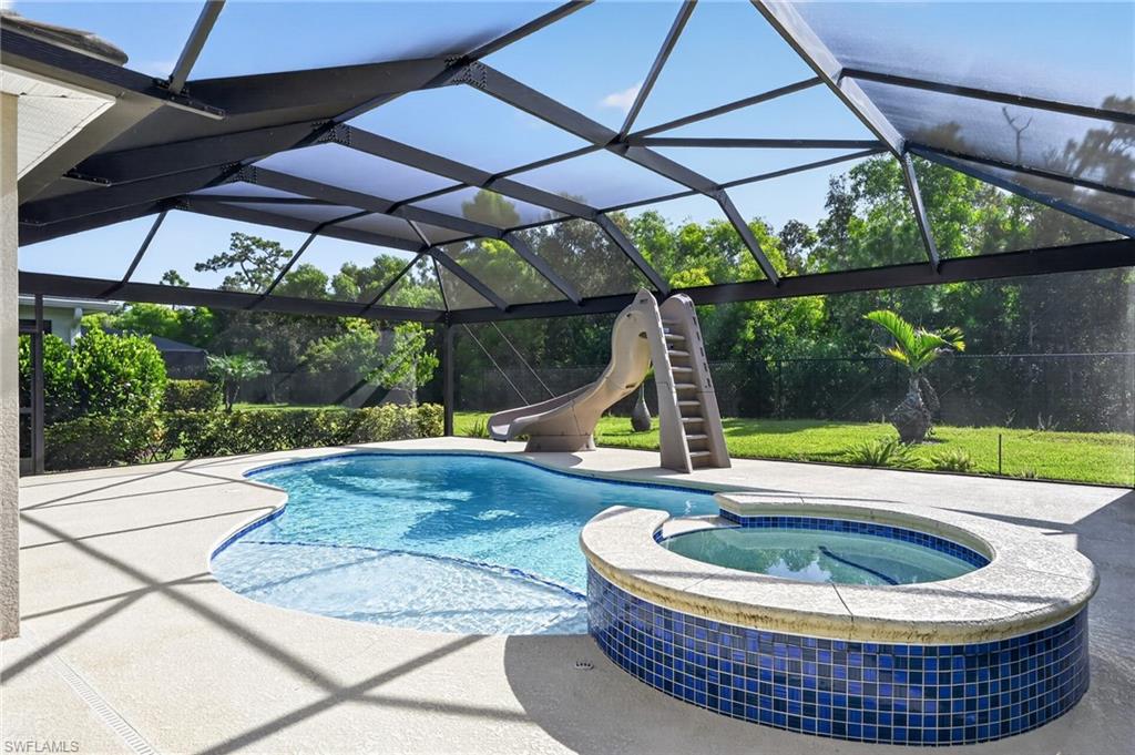 Screened enclosure featuring a freeform swimming pool, integrated spa with blue tile surround, and concrete decking