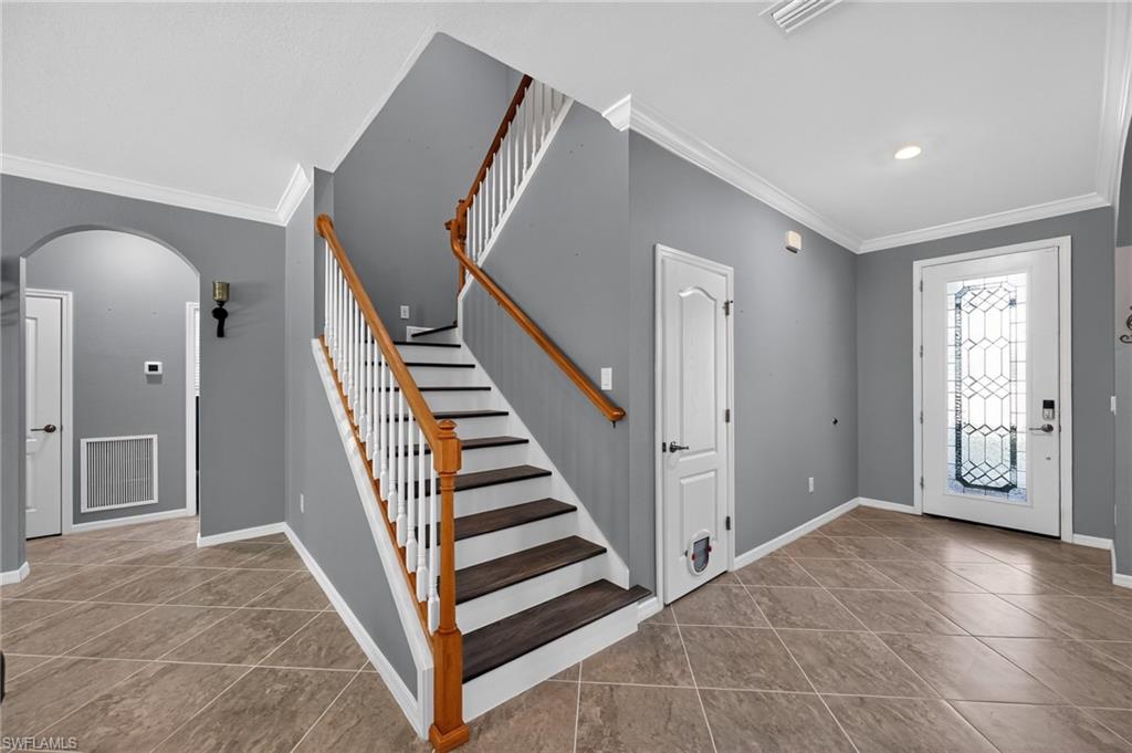 Tile flooring, white crown molding, wood-finish stair treads, decorative glass front door, and an arched hallway entry