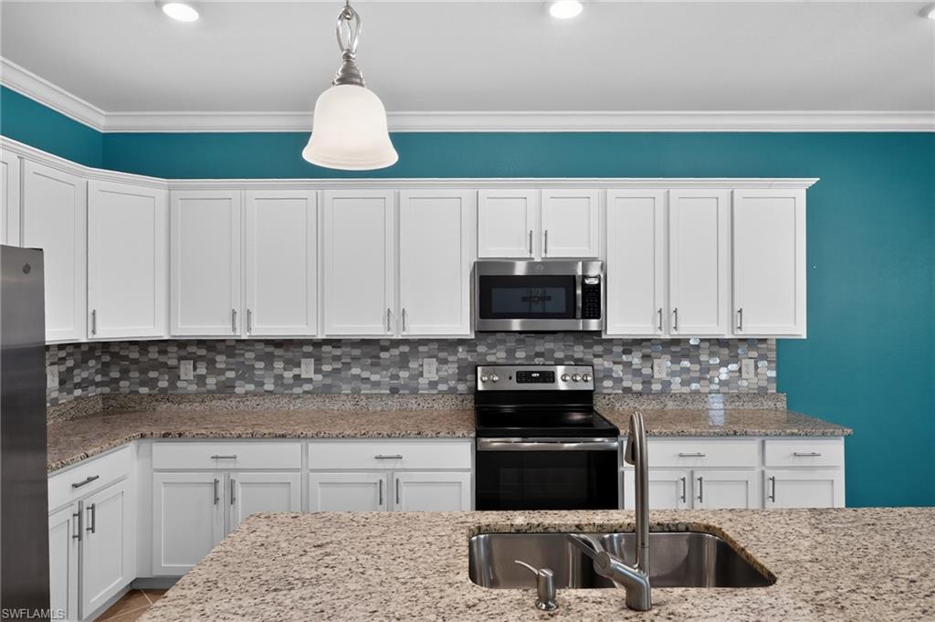 Chef's kitchen featuring white shaker cabinetry, stainless steel appliances including dual ovens and a gas cooktop, granite countertops with undermount dual sink, and a mosaic tile backsplash