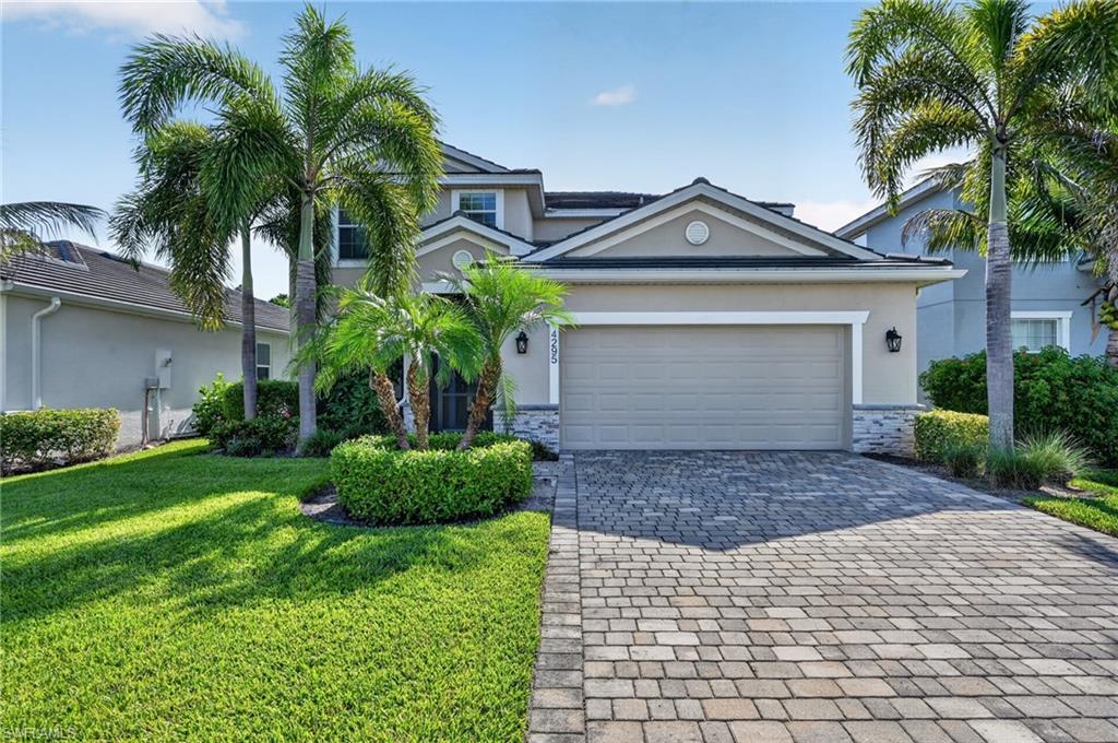 Stucco exterior with stone accenting, paver driveway, attached garage, and mature landscaping