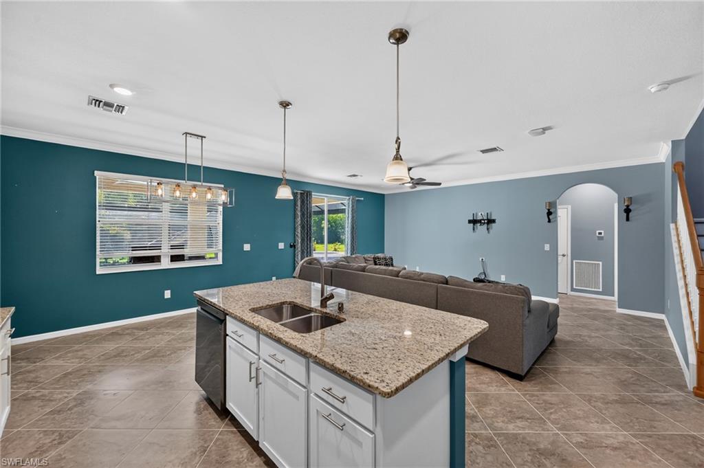 Kitchen island with granite countertop, stainless steel double sink, and pendant lighting