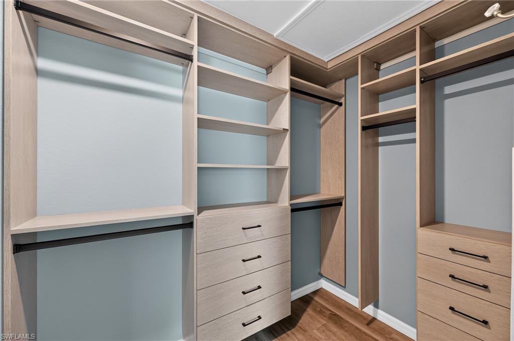 Luxurious walk-in closet featuring custom wood-finish cabinetry with multiple hanging rods, built-in shelving, and four deep drawers with metal hardware