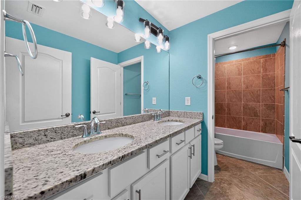 Master bathroom featuring dual vanities with speckled quartz countertops, white cabinetry with brushed nickel hardware, and a granite-topped counter surface