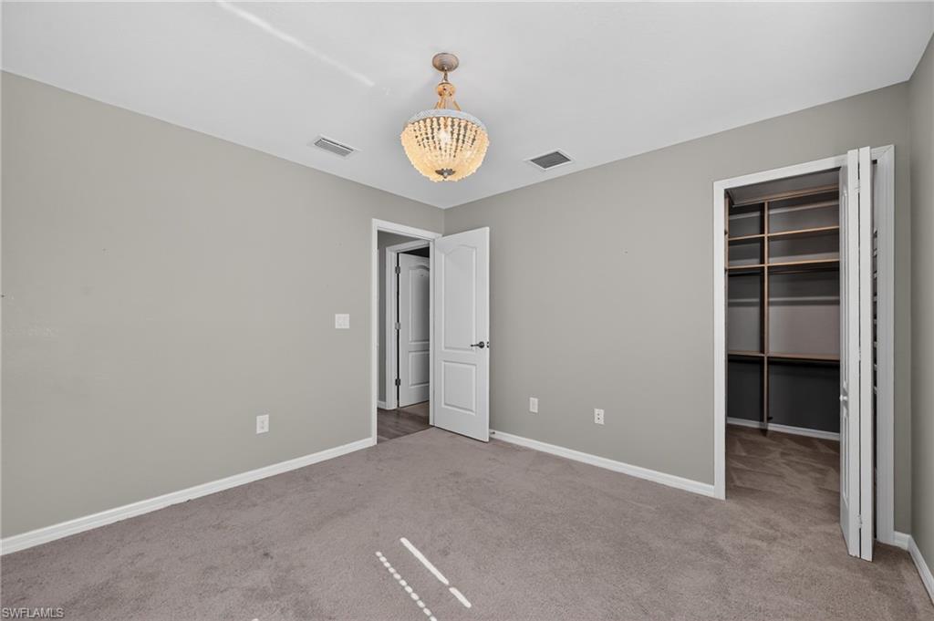 Neutral-toned wall paint, carpet flooring, a beaded chandelier, and a built-in closet system