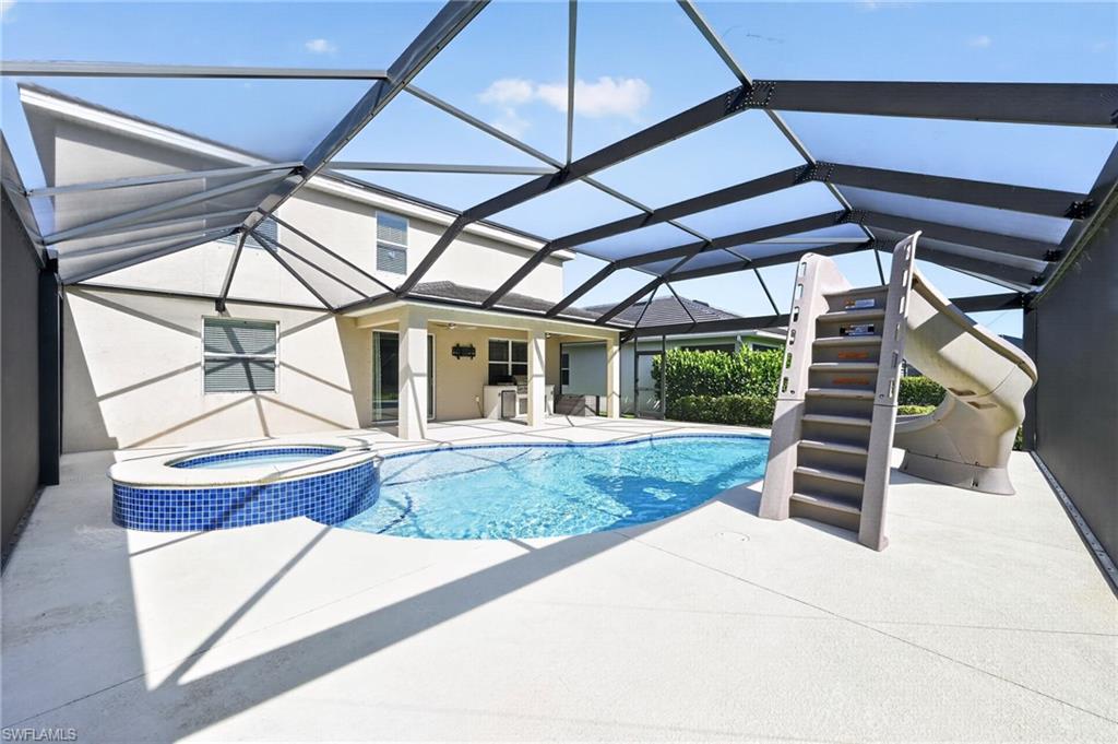 Screened-in outdoor pool area featuring a freeform pool, integrated spa with mosaic tile, and a pool slide