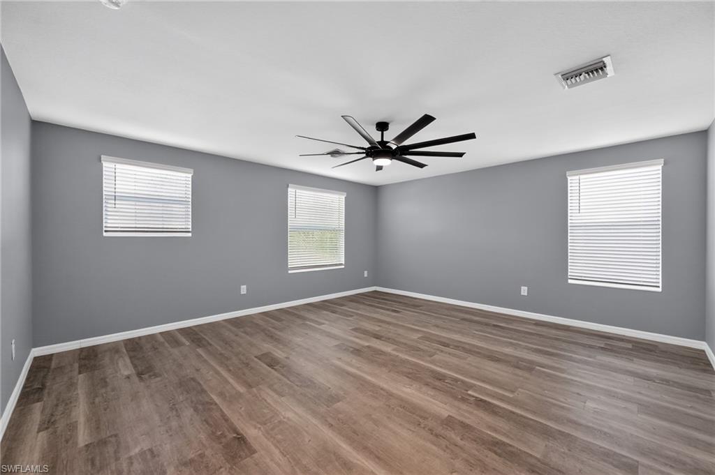Spacious room featuring light gray walls, wood-finish flooring, multiple windows with blinds, and a black ceiling fan with integrated lighting