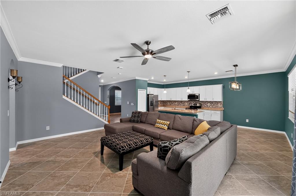 Open-concept living space with tile flooring, a staircase with wood railing, recessed lighting, and a ceiling fan, featuring a kitchen with white cabinetry and a tile backsplash