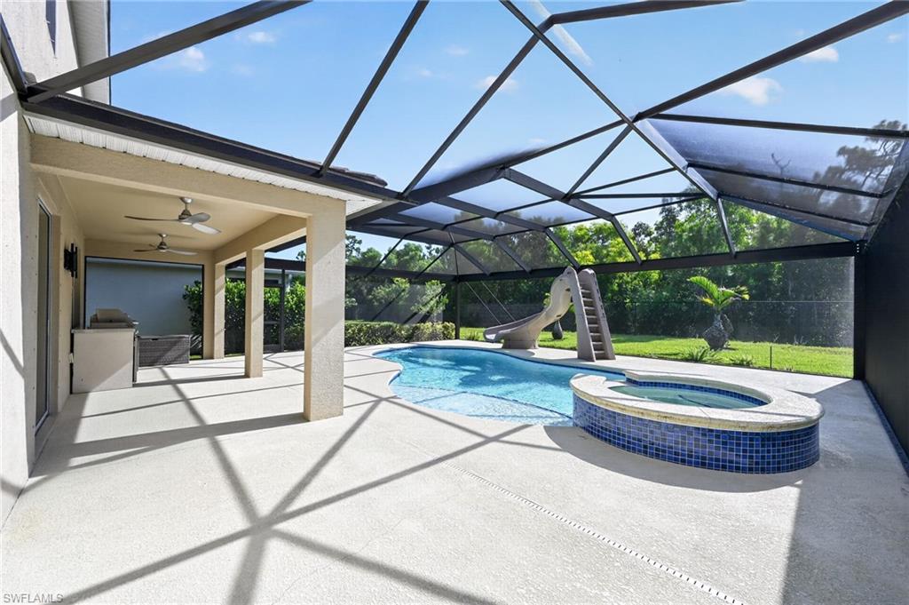 Screened-in outdoor living space featuring a swimming pool, integrated spa with blue mosaic tile, covered patio, and outdoor kitchen with built-in cabinetry