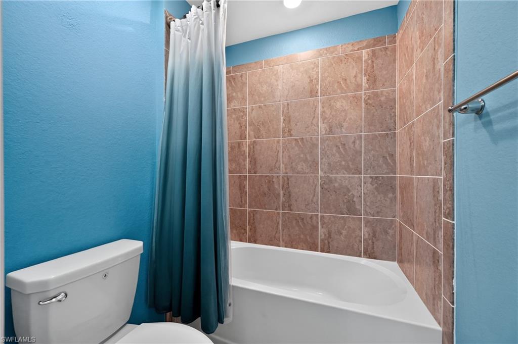 Bright bathroom featuring vibrant blue painted walls, a ceramic tile surround in warm earth tones, and a white porcelain bathtub with integrated shower