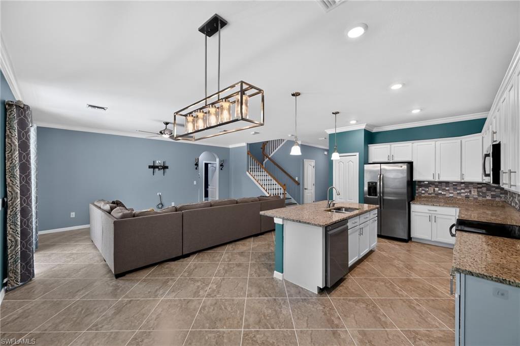 Open-concept living and kitchen featuring wood-finish flooring throughout, custom cabinetry with white and teal finishes, stainless steel appliances, a large island with wood countertop, pendant lighting, and a coffered ceiling with recessed lighting