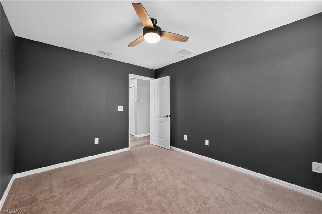 Neutral tone walls with contrasting dark accent wall, ceiling fan with integrated lighting, and neutral tone carpeting