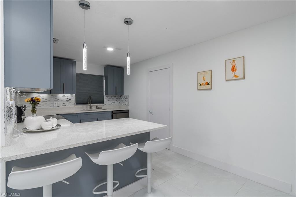 Kitchen featuring light gray cabinetry, white countertops, two pendant lights, and a mosaic tile backsplash